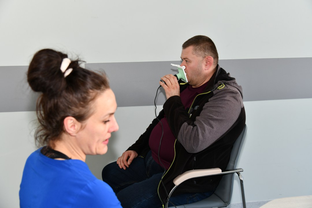 Lekarka wykonuje badanie spirometryczne siedzącemu naprzeciw niej mężczyźnie.