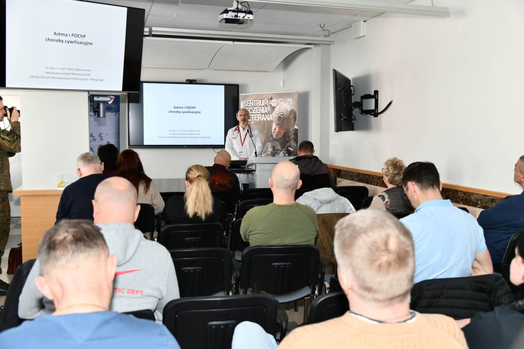 Ujęcie z tyłu sali na słuchaczy wykładu i prowadzącego wykład Piotra Dąbrowieckiego.