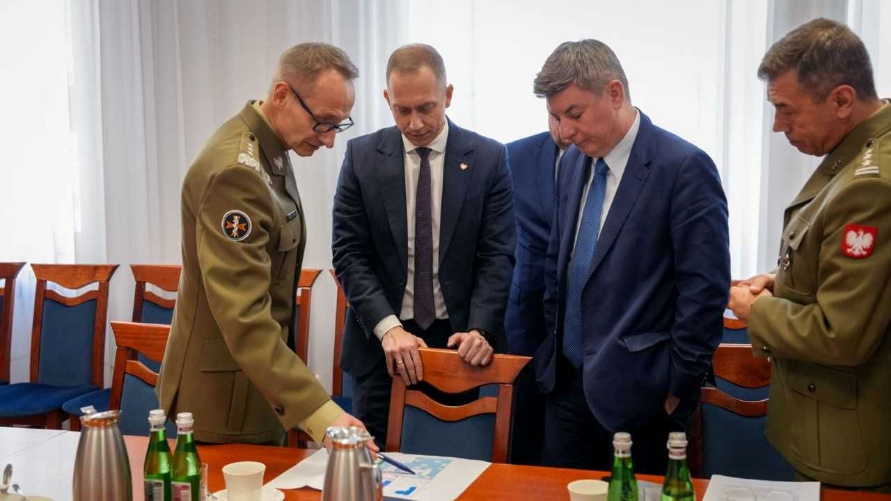 Cezary Tomczyk, Jan Grabiec, Roman Smogorzewsk, Grzegorz Gielerak stoją przy stole i omawiają leżący na nim dokument.