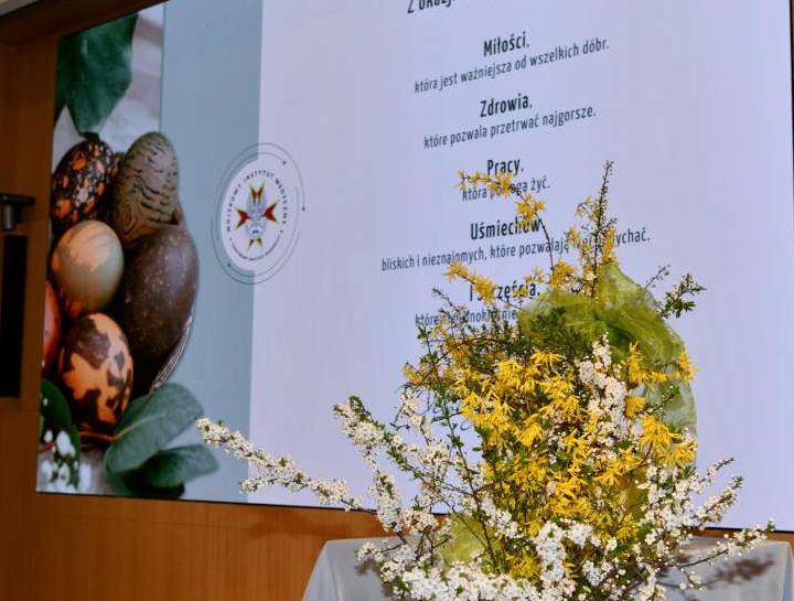 Stroik wielkanocny na auli WIM za nim wyświetlone na ekranie życzenia wielkanocne.