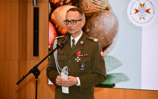 Grzegorz Gielerak przy mikrofonie, za nim na ekranie wyświetlone życzenia wielkanocne.