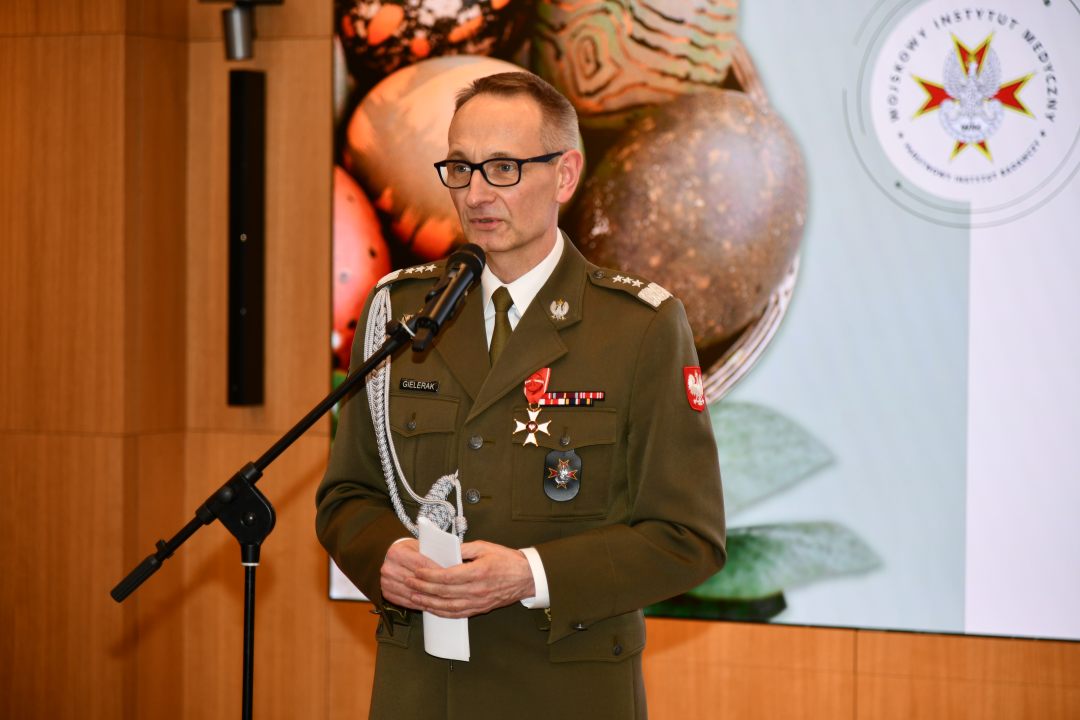 Grzegorz Gielerak przy mikrofonie, za nim na ekranie wyświetlone życzenia wielkanocne.