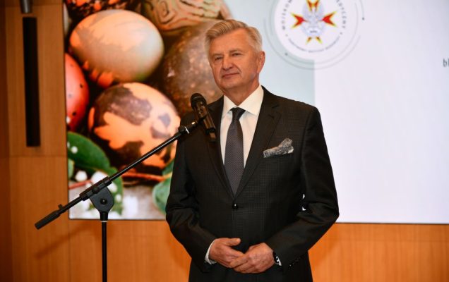 Stanisław Wziątek przy mikrofonie, za nim na ekranie wyświetlone życzenia wielkanocne.