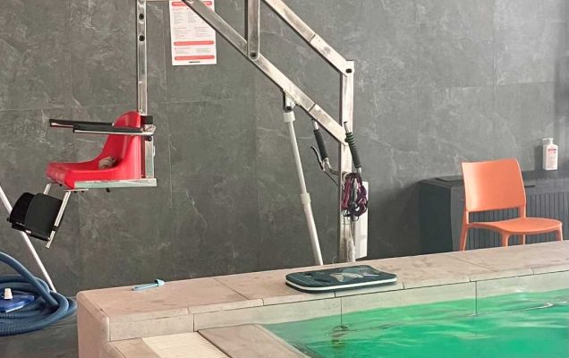 Wysięgnik z krzesełkiem przy basenie rehabilitacyjnym.