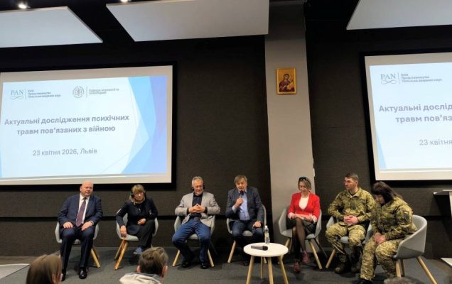 Uczestnicy panelu dyskusyjnego na sali konferencyjnej. Za nimi dwa wyświetlacze z treściami konferencji.