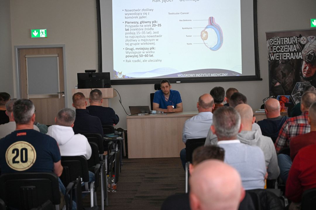 Siedzący słuchacze podczas wykładu. Za plecami prelegenta na wyświetlaczu plansza prezentacji.