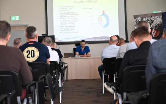 Siedzący słuchacze podczas wykładu. Za plecami prelegenta na wyświetlaczu plansza prezentacji.