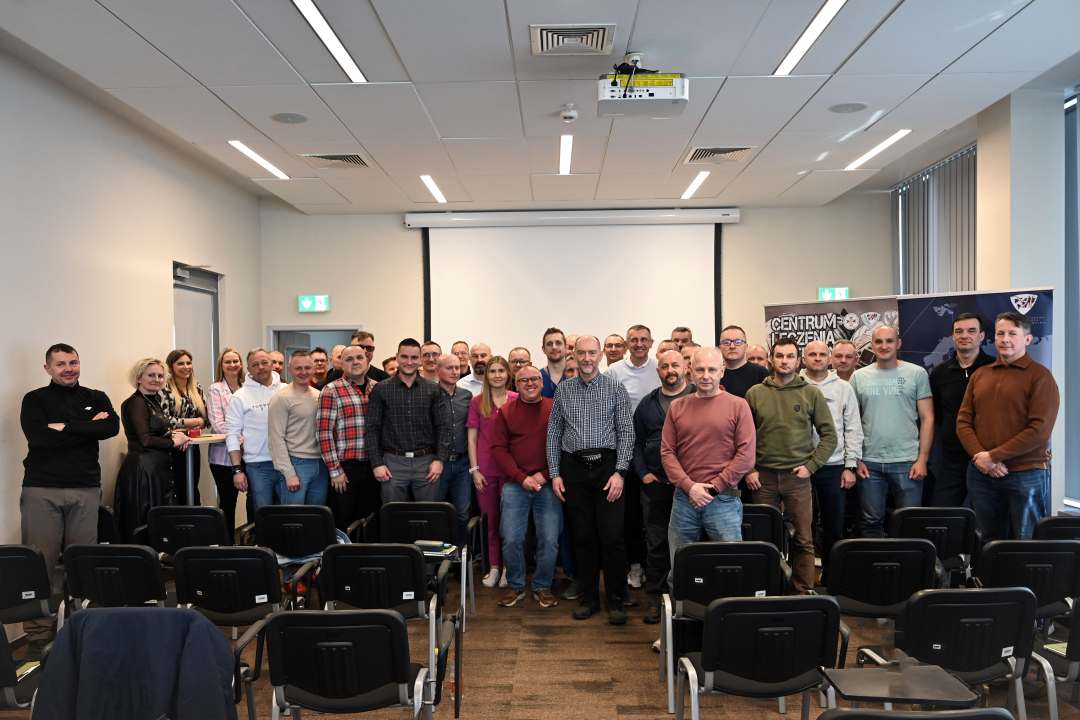 Zdjęcie grupowe stojących uczestników wydarzenia na sali wykładowej.