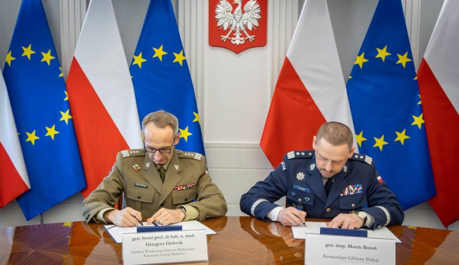 Grzegorz Gielerak i Roman Smogorzewski podpisują przy stole listy intencyjne. Za ich plecami godło RP oraz flagi UE i RP.