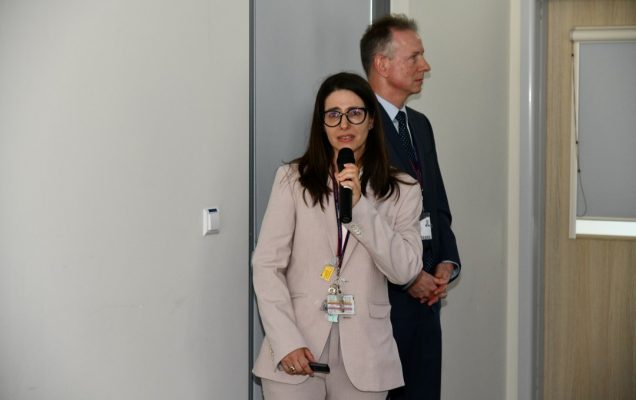 Prelegentka z mikrofonem w reku prowadzi prezentację.