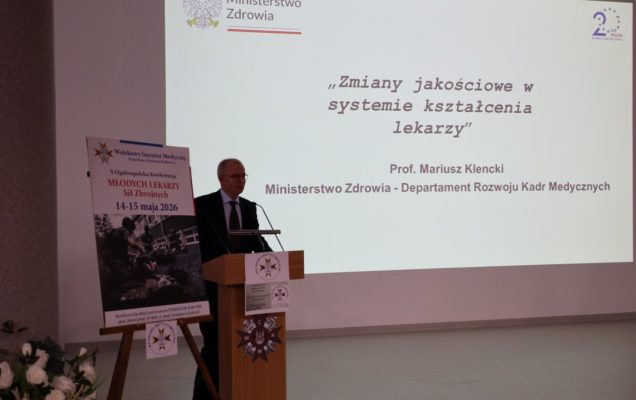 Prelegent przy mównicy za jego plecami wyświetlony slajd prezentacji.