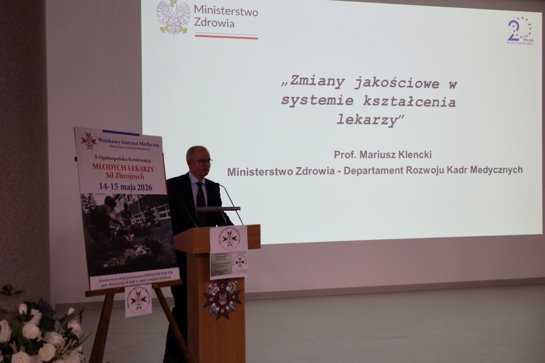 Prelegent przy mównicy za jego plecami wyświetlony slajd prezentacji.