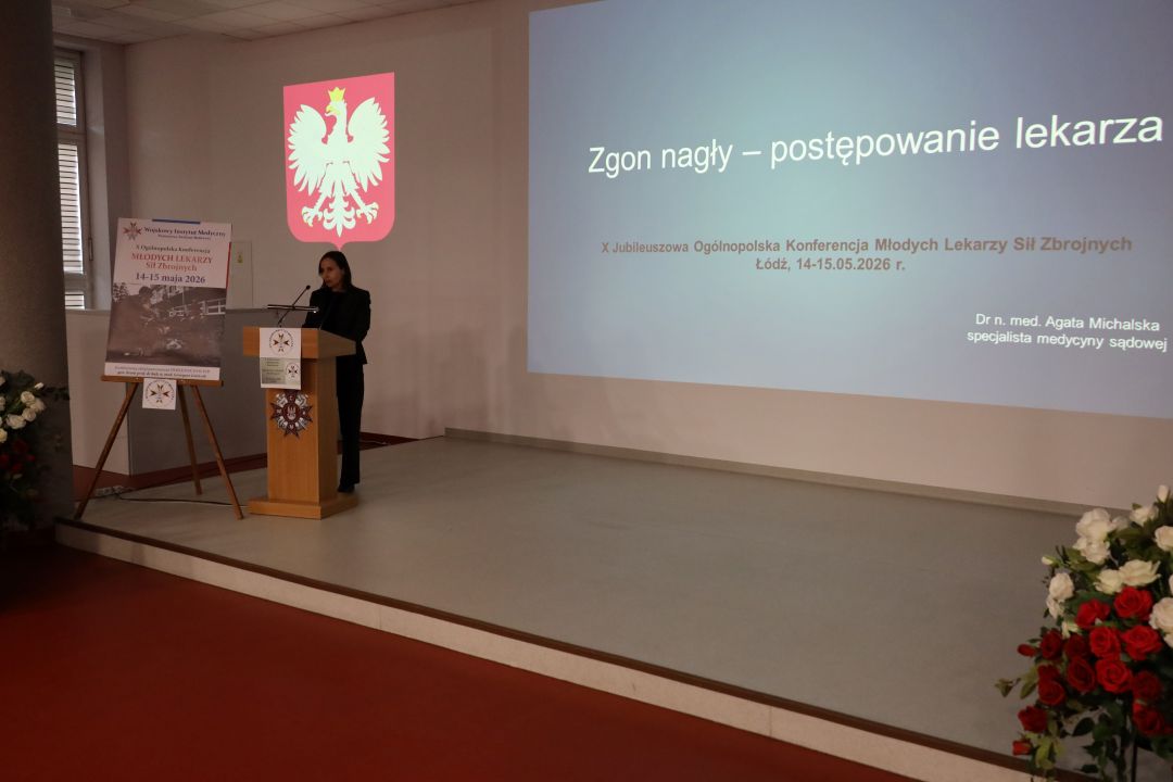 Prelegent przy mównicy za jego plecami wyświetlony slajd prezentacji.
