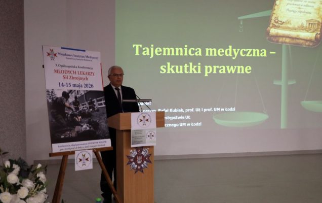 Prelegent przy mównicy za jego plecami wyświetlony slajd prezentacji.