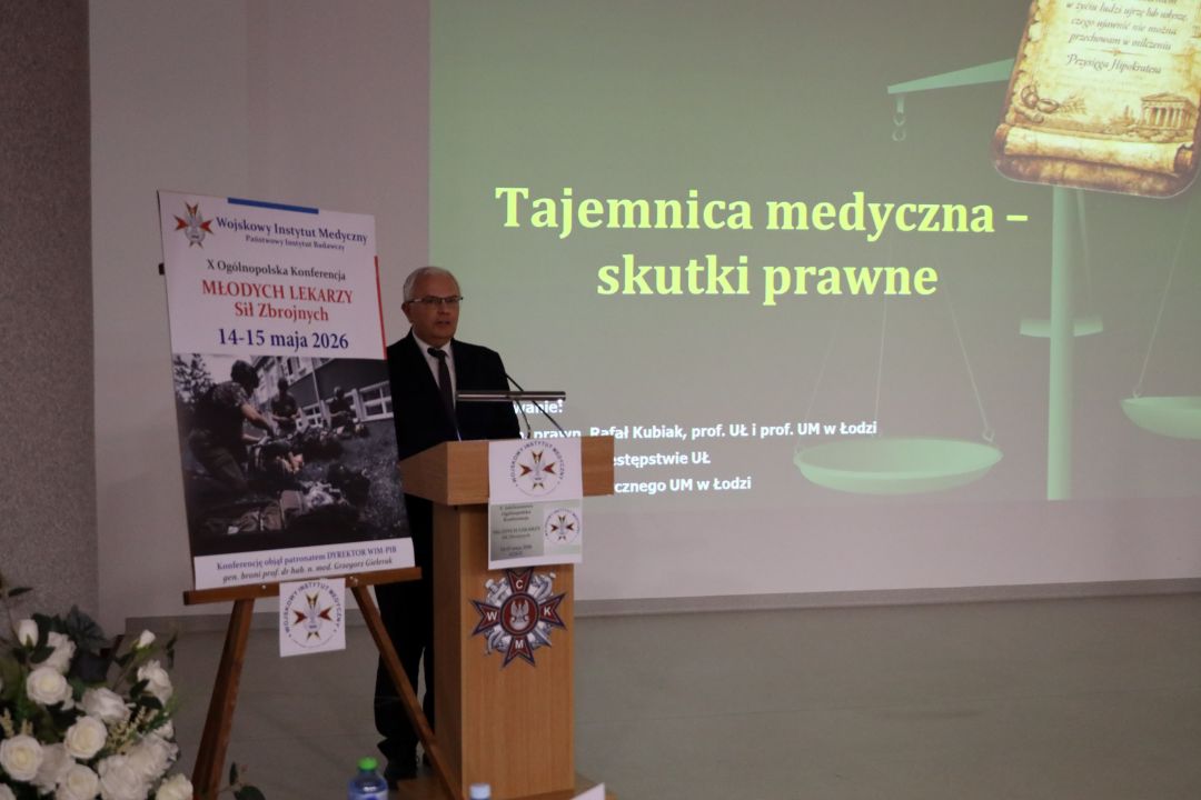 Prelegent przy mównicy za jego plecami wyświetlony slajd prezentacji.