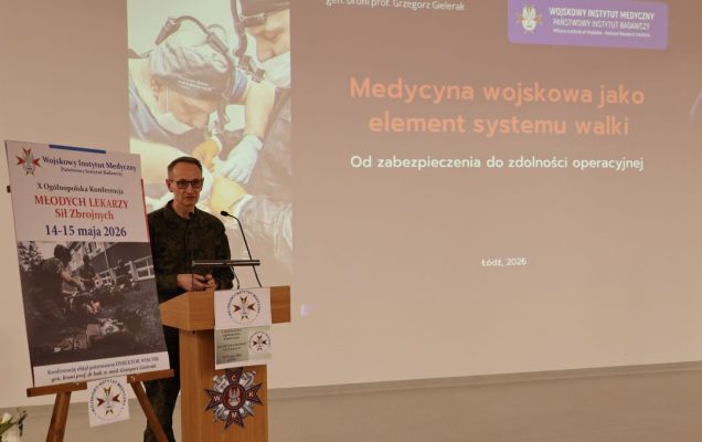 Dyrektor WIM przy mównicy, za jego plecami na ekranie slajd z konferencji.