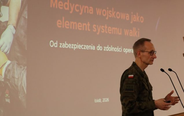 Dyrektor WIM przy mównicy, za jego plecami na ekranie slajd z konferencji.