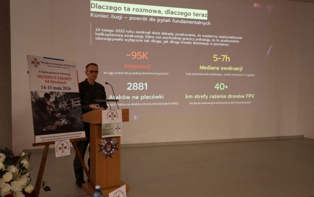 Dyrektor WIM przy mównicy, za jego plecami na ekranie slajd z konferencji.