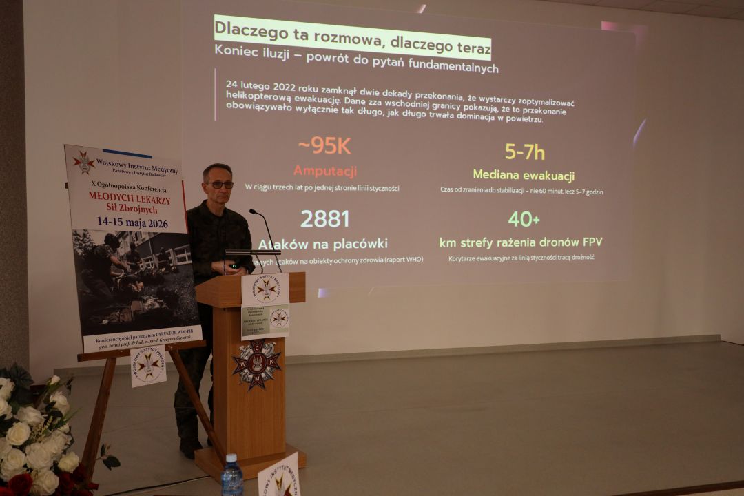 Dyrektor WIM przy mównicy, za jego plecami na ekranie slajd z konferencji.