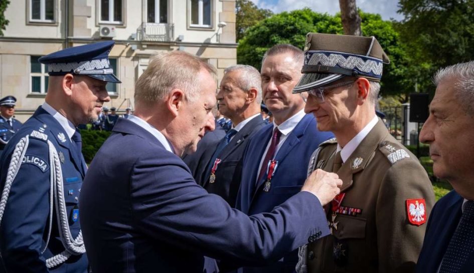 Czesław Mroczek przypina Dyrektorowi WIM medal przed gmachem policji.