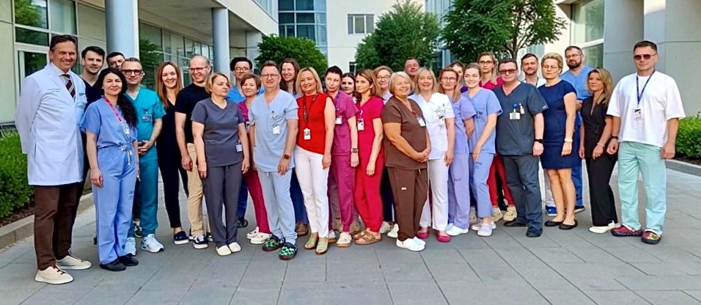 Pracownicy Kliniki Kardiochirurgii WIM-PIB pozują do zdjęcia przed budynkiem kliniki.