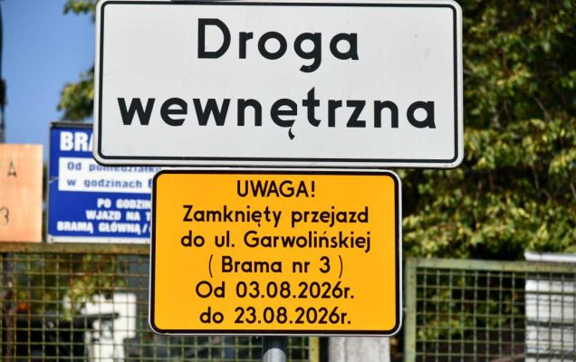 Dwa polskie znaki drogowe na słupku – biały z napisem „Droga wewnętrzna” oraz żółty ostrzegawczy o zamknięciu przejazdu do ul. Garwolińskiej (Brama nr 3) w dniach 03.08.2026–23.08.2026, na tle ogrodzenia i zieleni.