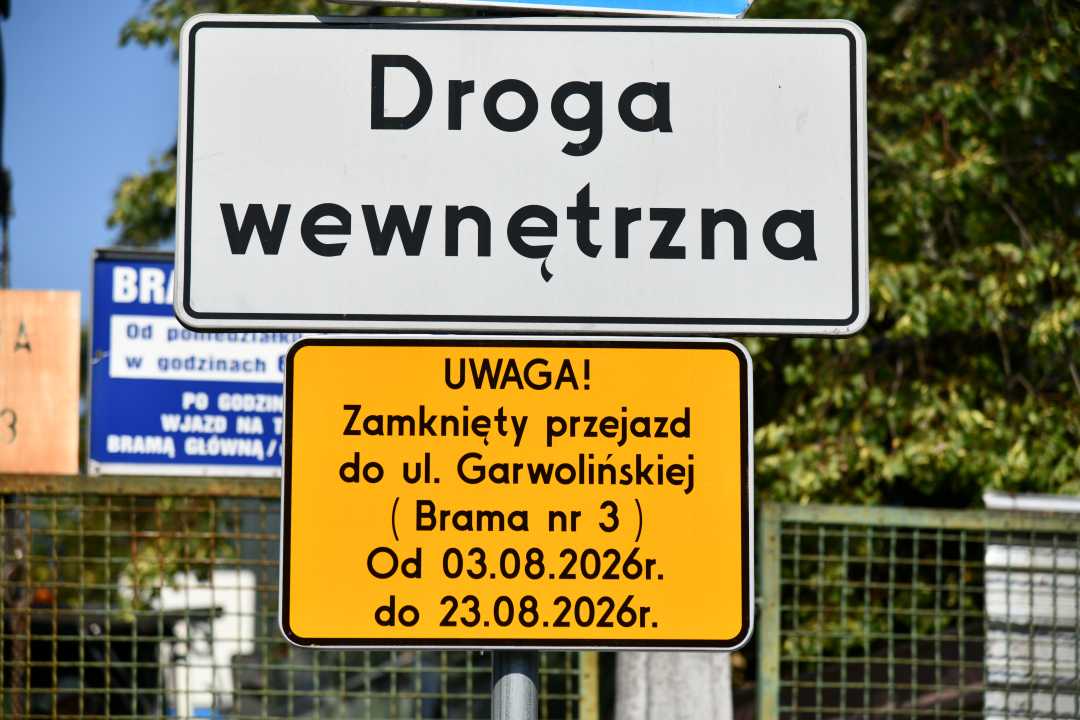 Dwa polskie znaki drogowe na słupku – biały z napisem „Droga wewnętrzna” oraz żółty ostrzegawczy o zamknięciu przejazdu do ul. Garwolińskiej (Brama nr 3) w dniach 03.08.2026–23.08.2026, na tle ogrodzenia i zieleni.