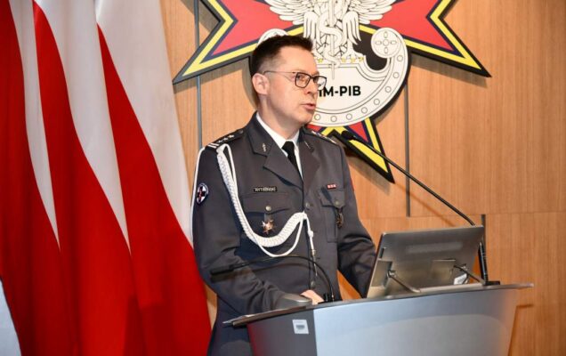 Jarosław Rytwiński przy mównicy. Za nim trzy flagi Polski i logotyp WIM.