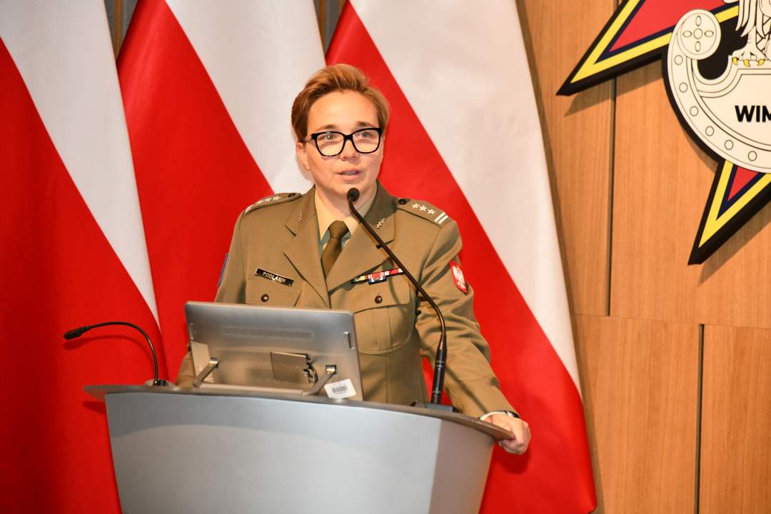 płk Anita Podlasin - Dyrektor Departamentu Wojskowej Służby Zdrowia przy mównicy. Za nim trzy flagi Polski i logotyp WIM.