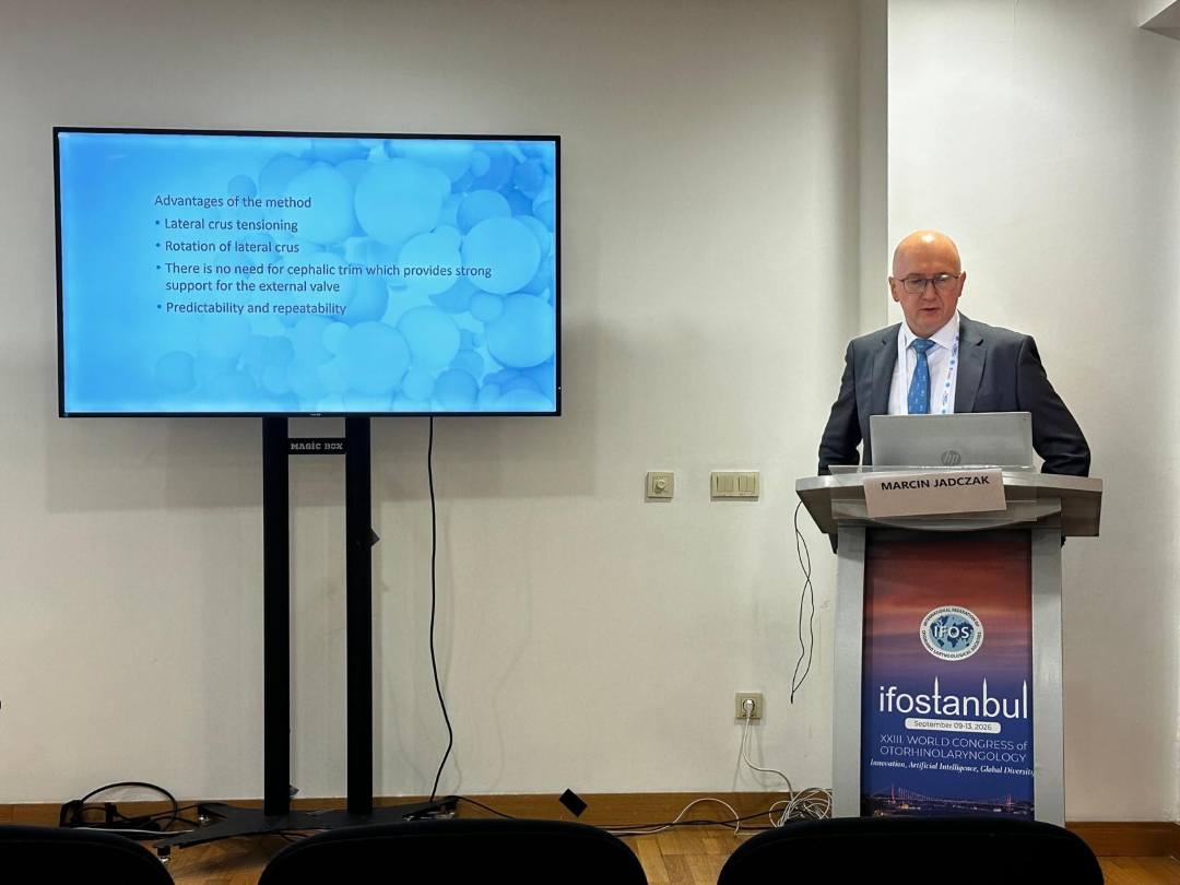 Prelegent przy mównicy podczas prelekcji. Obok niego na ekranie wyświetlony slajd z konferencji.