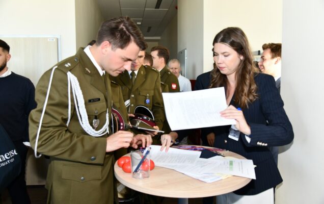 Stoisko z ankietami dla uczestników inauguracji. Młody lekarz uzupełnia ankietę.