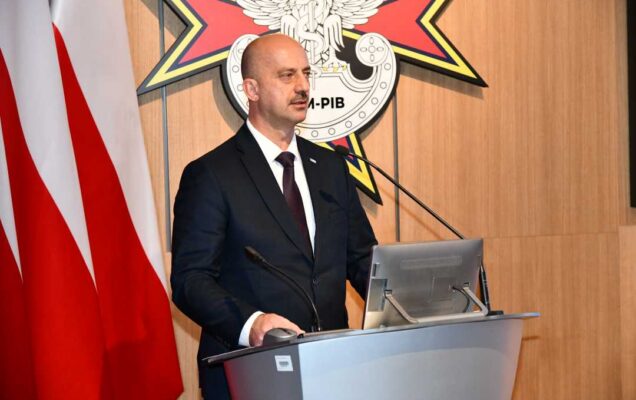 Mirosław Bryś przy mównicy. Za jego plecami flaga Polski i logotyp WIM-PIB.