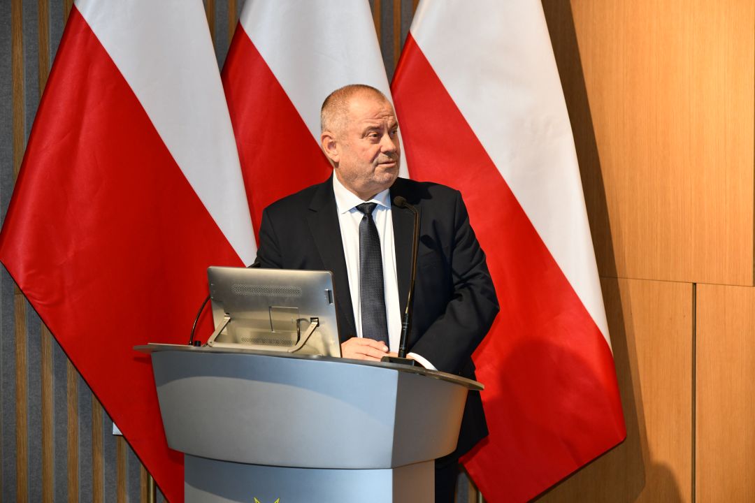 Alojzy Nowak przy mównicy. Za jego plecami flaga Polski i logotyp WIM-PIB.