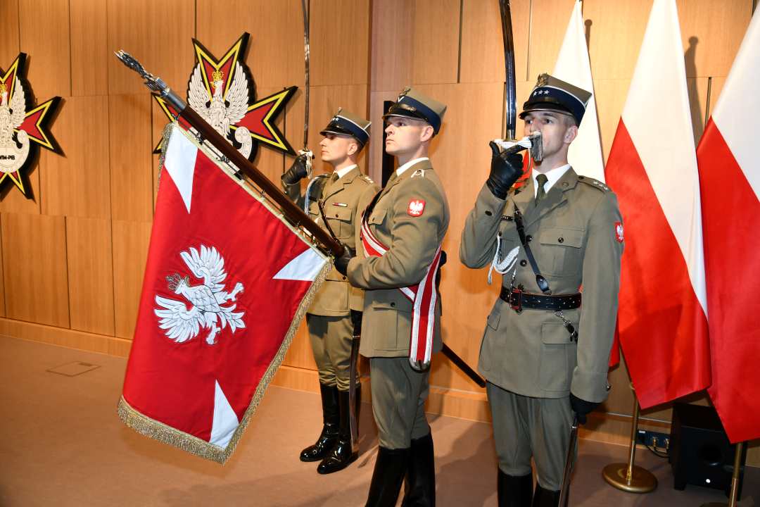 Poczet sztandarowy. Trzech żołnierzy prezentujących szble, jeden z nich trzyma sztandar.